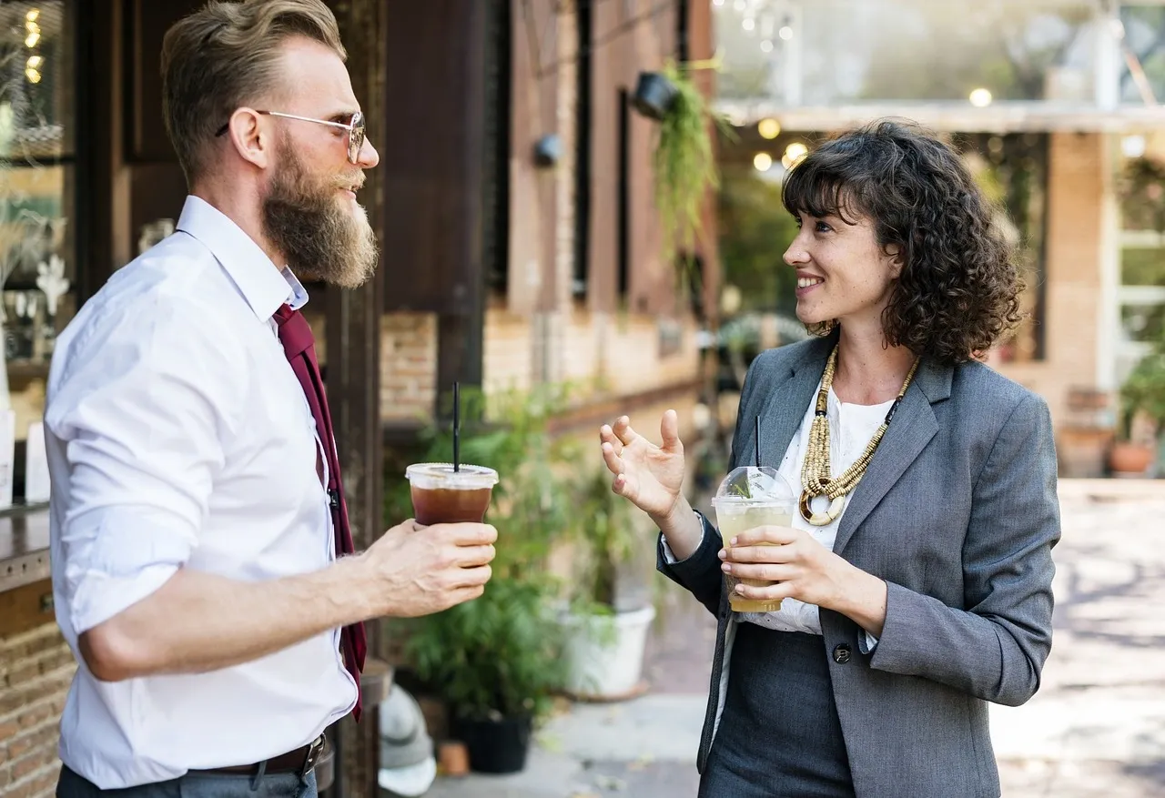 man with coffee talking to a woman in a business suit outside building
