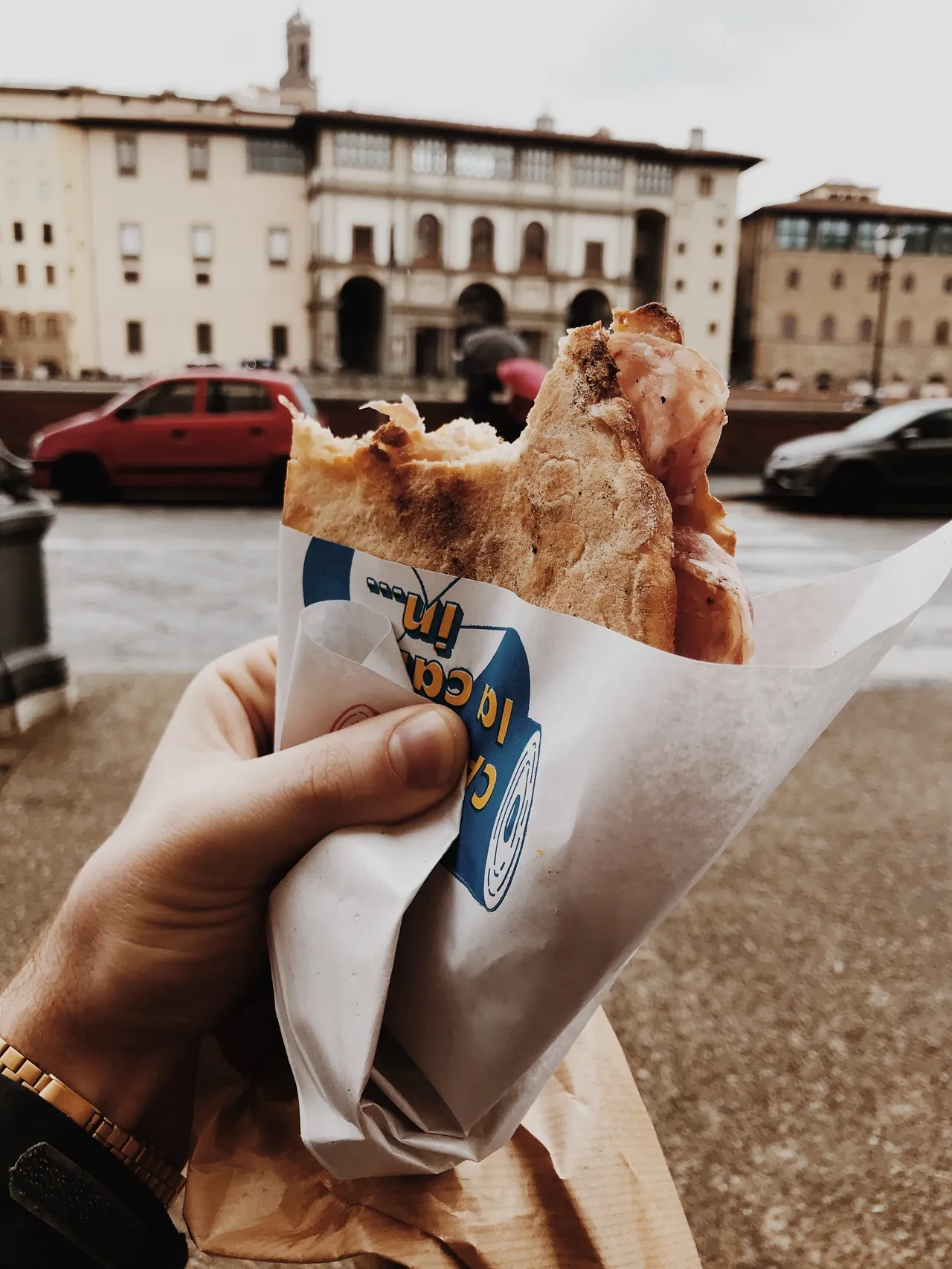 Hand holding with pita sandwich wrapped in paper in an outside plaza